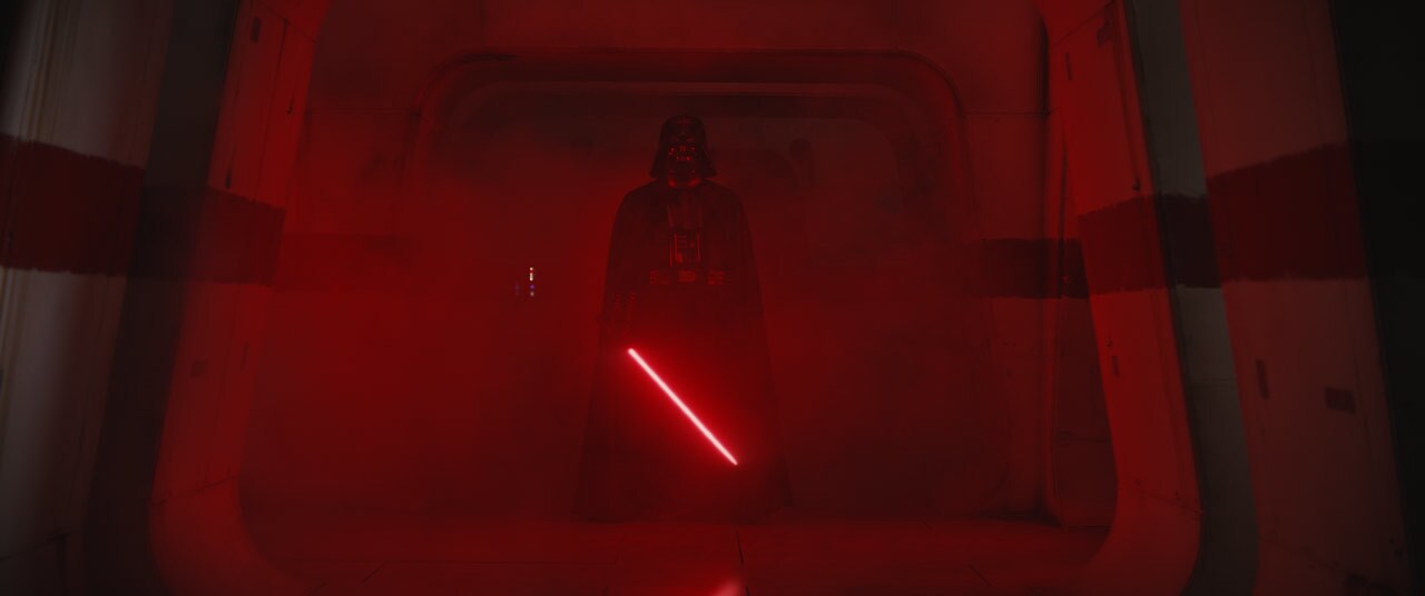 Darth Vader in the Rogue One corridor, holding his red lightsaber diagonally downward